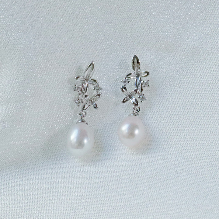 Pearlpals A pair of silver earrings with small flower designs, sparkling zircon stones, and a dangling freshwater pearl.