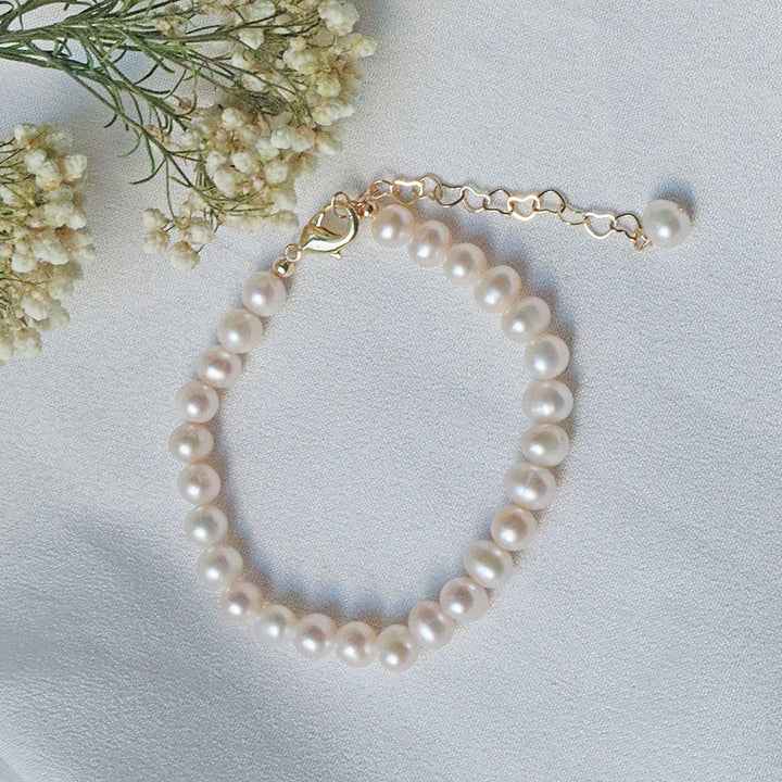 Pearlpals A gold-plated pearl bracelet with a simple design, heart-shaped chain, and a single pearl charm at the end