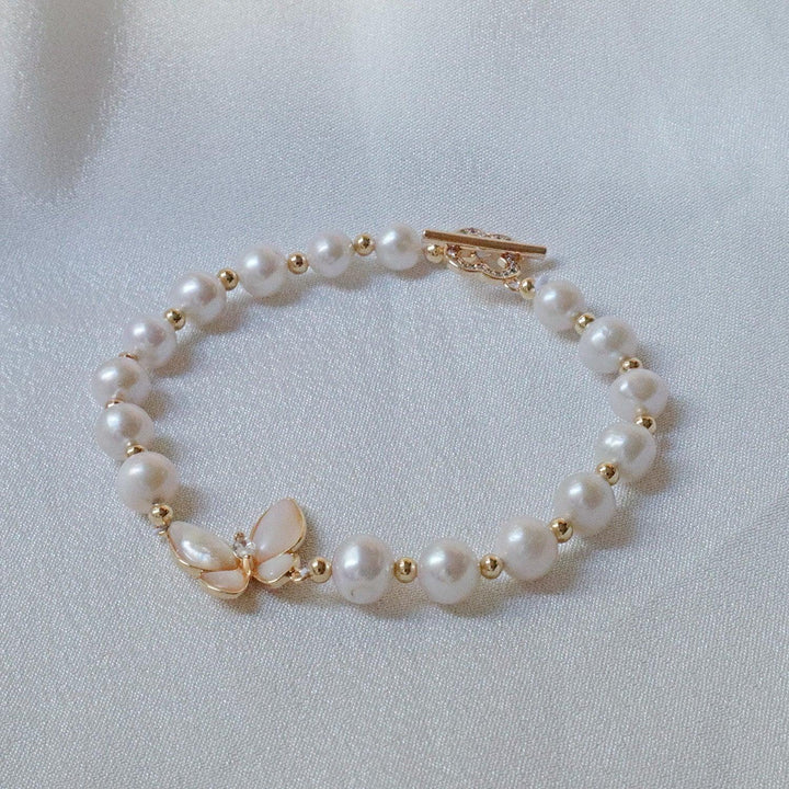 Pearlpals A gold-plated bracelet with pearls and gold beads, featuring a butterfly charm made of petal-shaped pearls