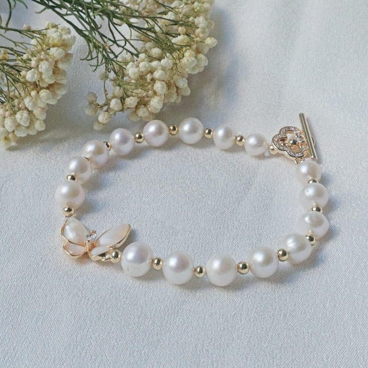 Pearlpals A gold-plated bracelet with pearls and gold beads, featuring a butterfly charm made of petal-shaped pearls