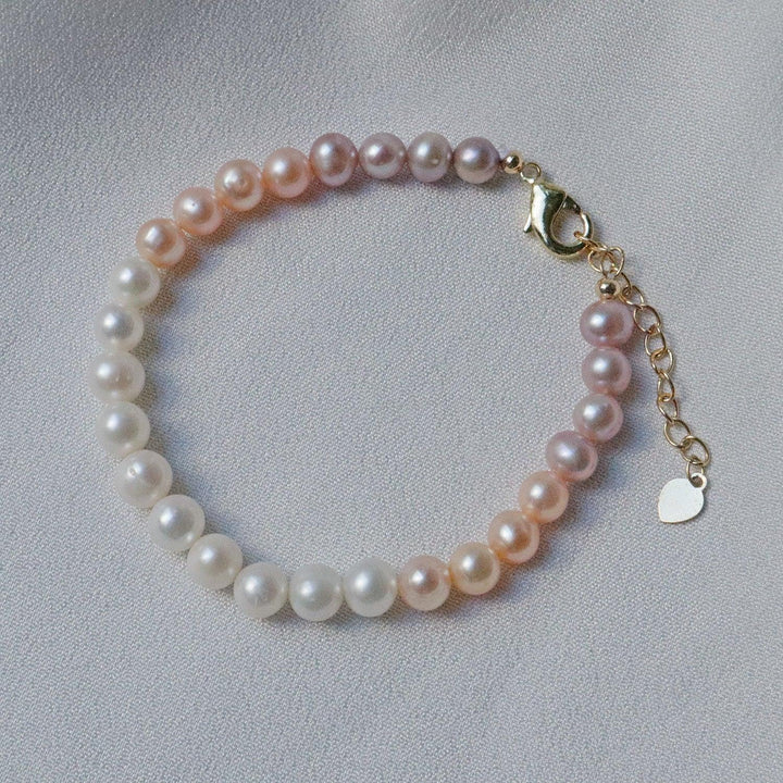 Pearlpals A gold-plated bracelet with gradient pearls transitioning from white to purple, displayed on a soft white fabric background.