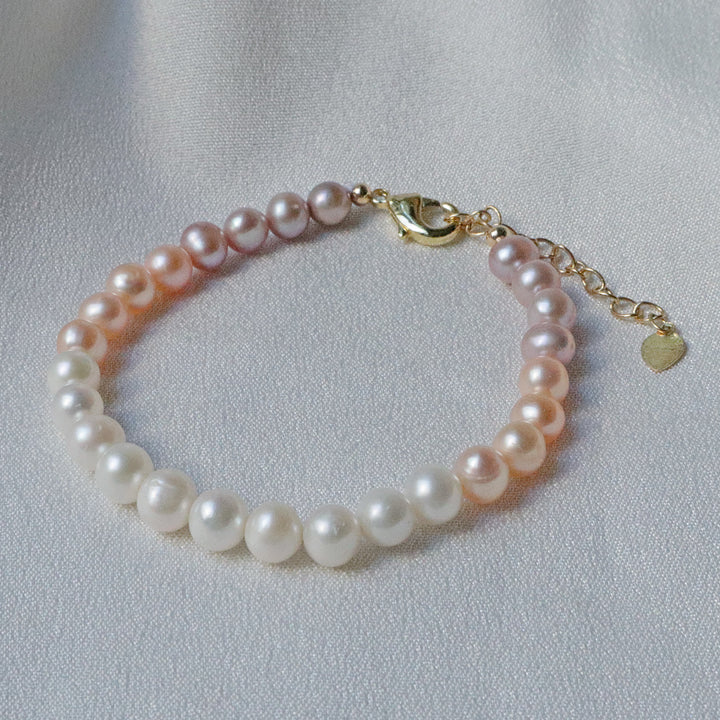 Pearlpals A gold-plated bracelet with gradient pearls transitioning from white to purple, displayed on a soft white fabric background.