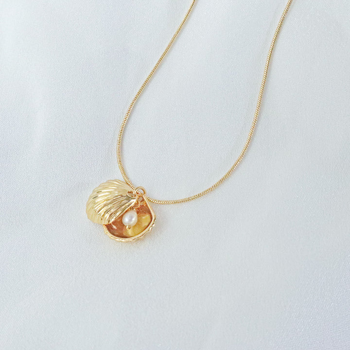 Gold-plated necklace with a shell-shaped pendant and a pearl inside, hanging on a gold chain
