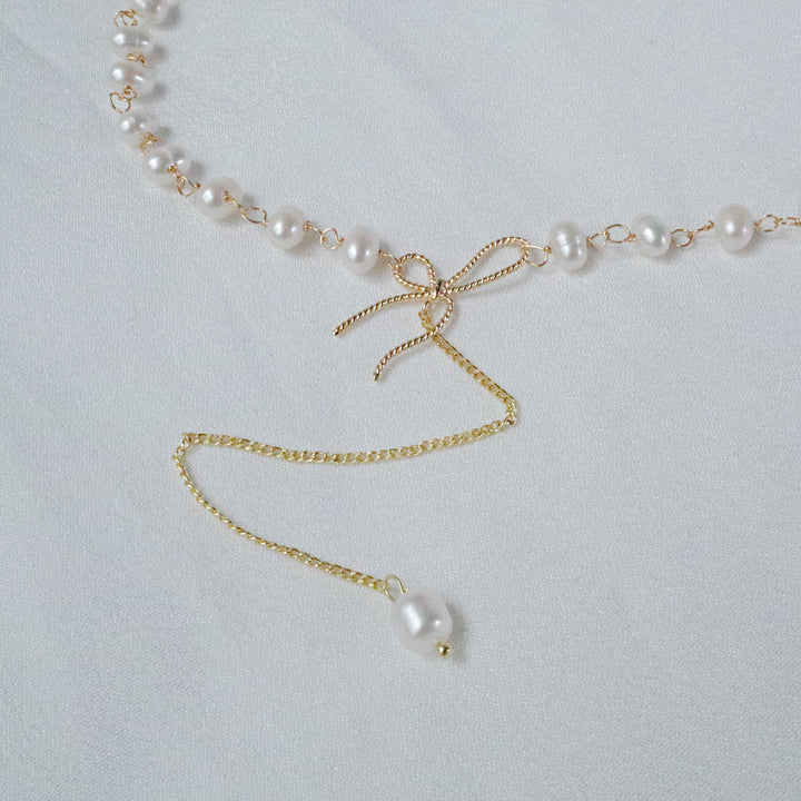 Gold-plated choker necklace with uniquely shaped pearls, a bow, and a long chain drop with a single pearl