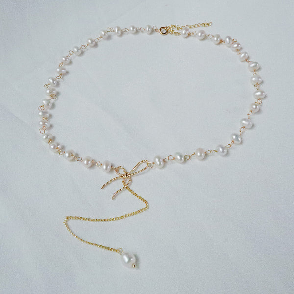 Gold-plated choker necklace with uniquely shaped pearls, a bow, and a long chain drop with a single pearl