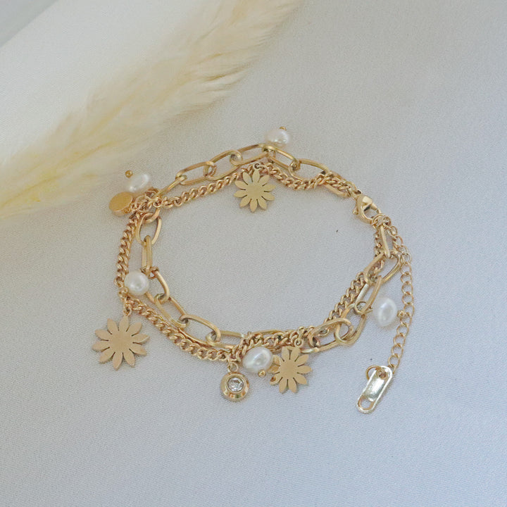 Pearlpals A double chains stainless steel bracelet with pearls and vintage-inspired charms, including flowers and geometric shapes, displayed on a soft white fabric background.