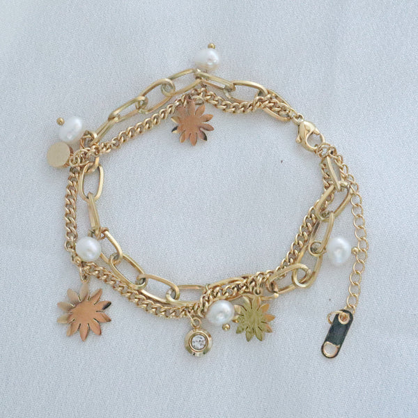 Pearlpals A double chains stainless steel bracelet with pearls and vintage-inspired charms, including flowers and geometric shapes, displayed on a soft white fabric background.